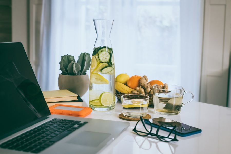 Laptop on a desk with infused water, fruit and herbal tea